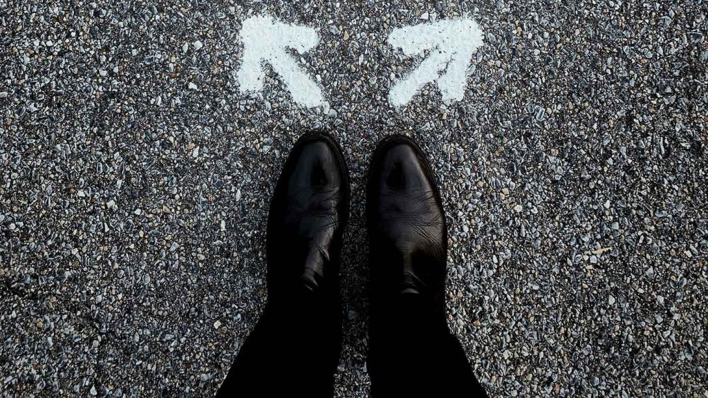 Polished black shoes stand on concrete in front of two arrows point in opposite directions